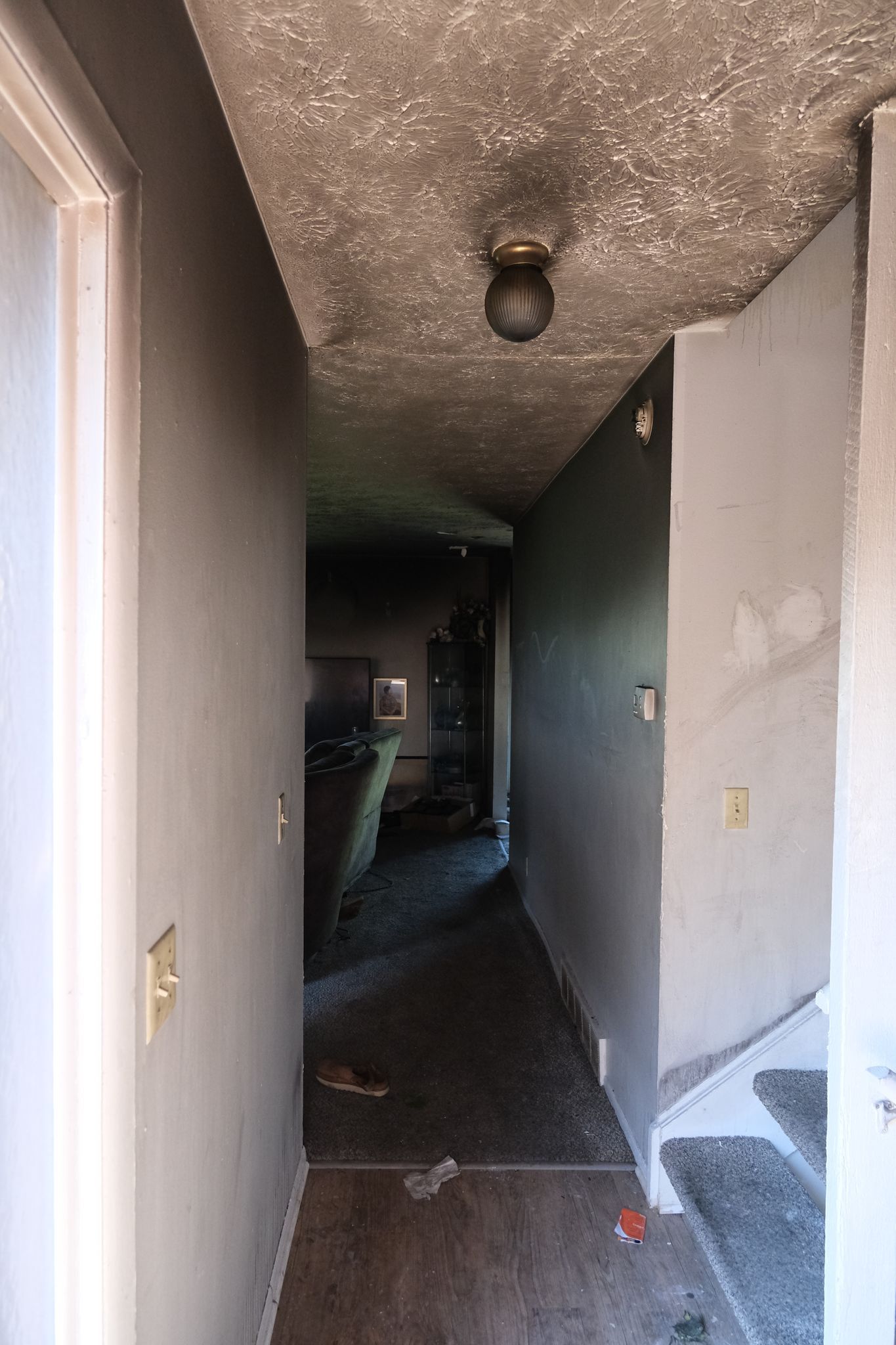 Hallway heavily damaged by fire, with charred ceiling and walls; debris on floor.