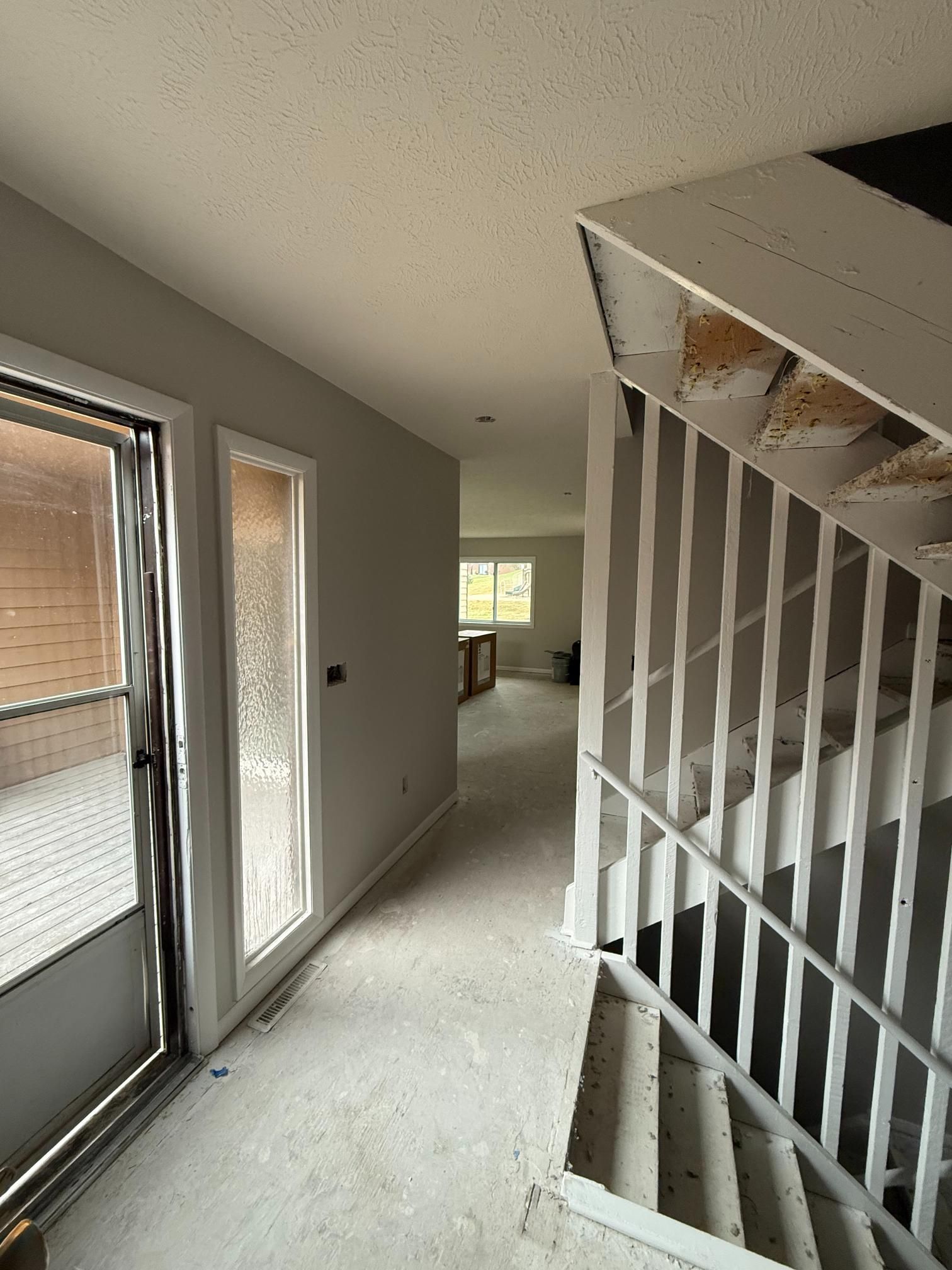 Interior view of a hallway with a staircase on the right and a door leading to a porch on the left.
