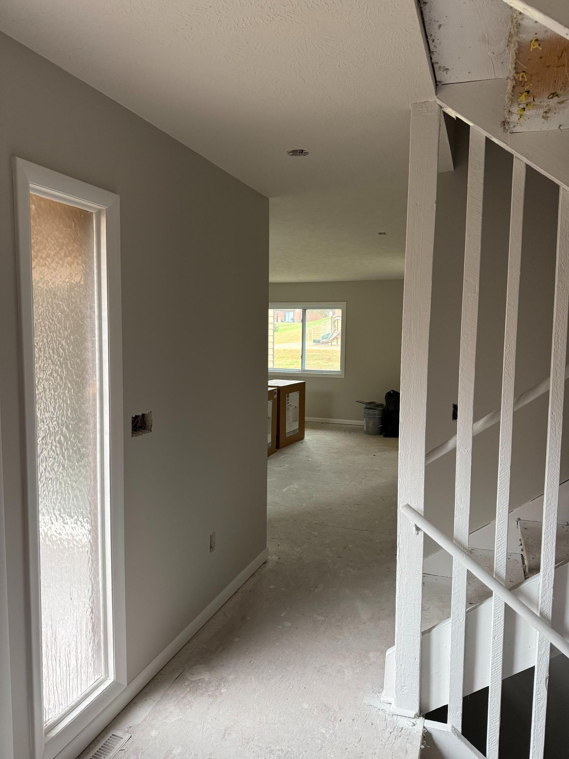 Hallway with front door, stairs, and view into a living space; walls are painted gray, with white door and stair accents.