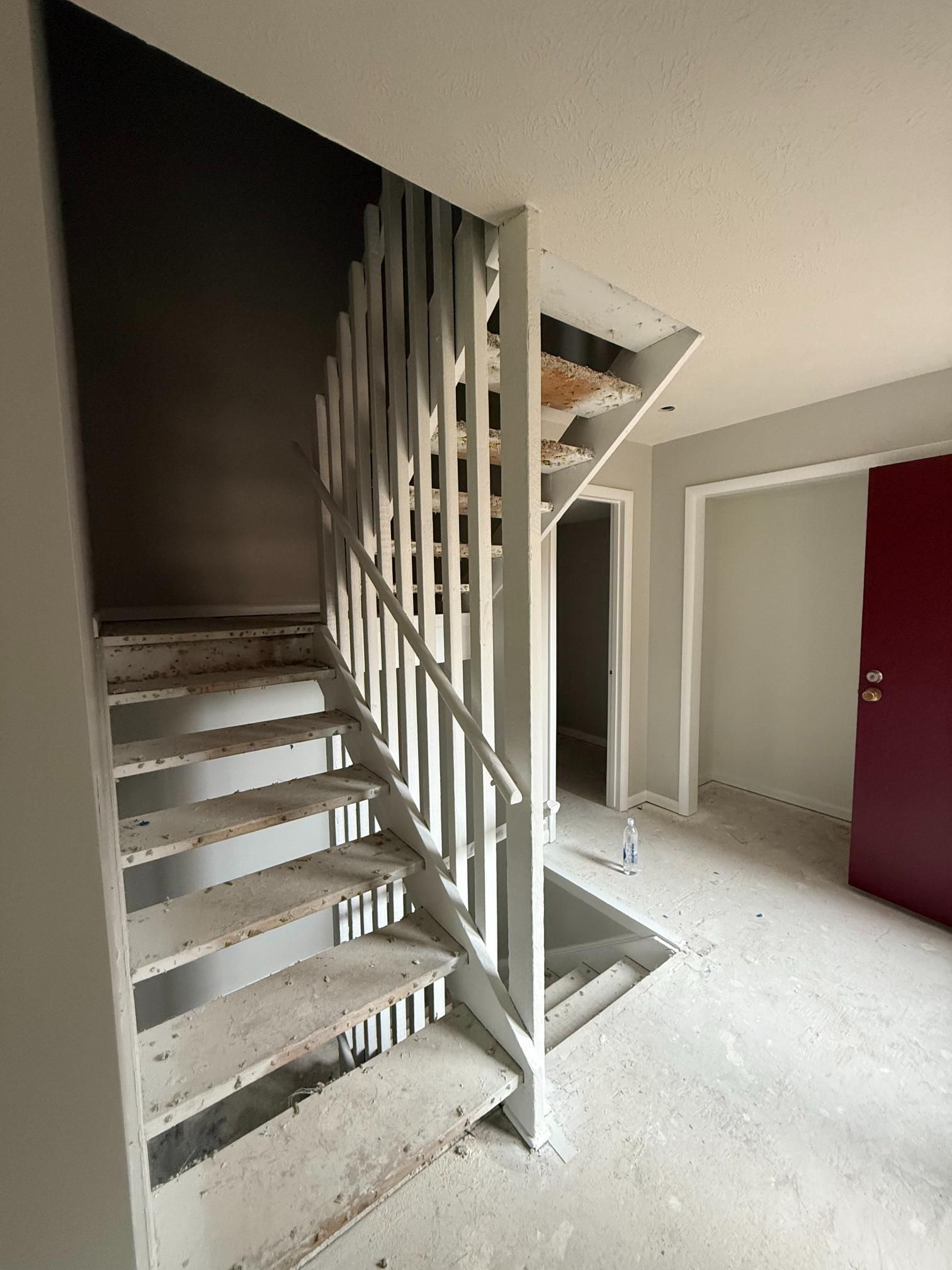 Concrete staircase with white railing and partial walls. A red door and doorway are visible.