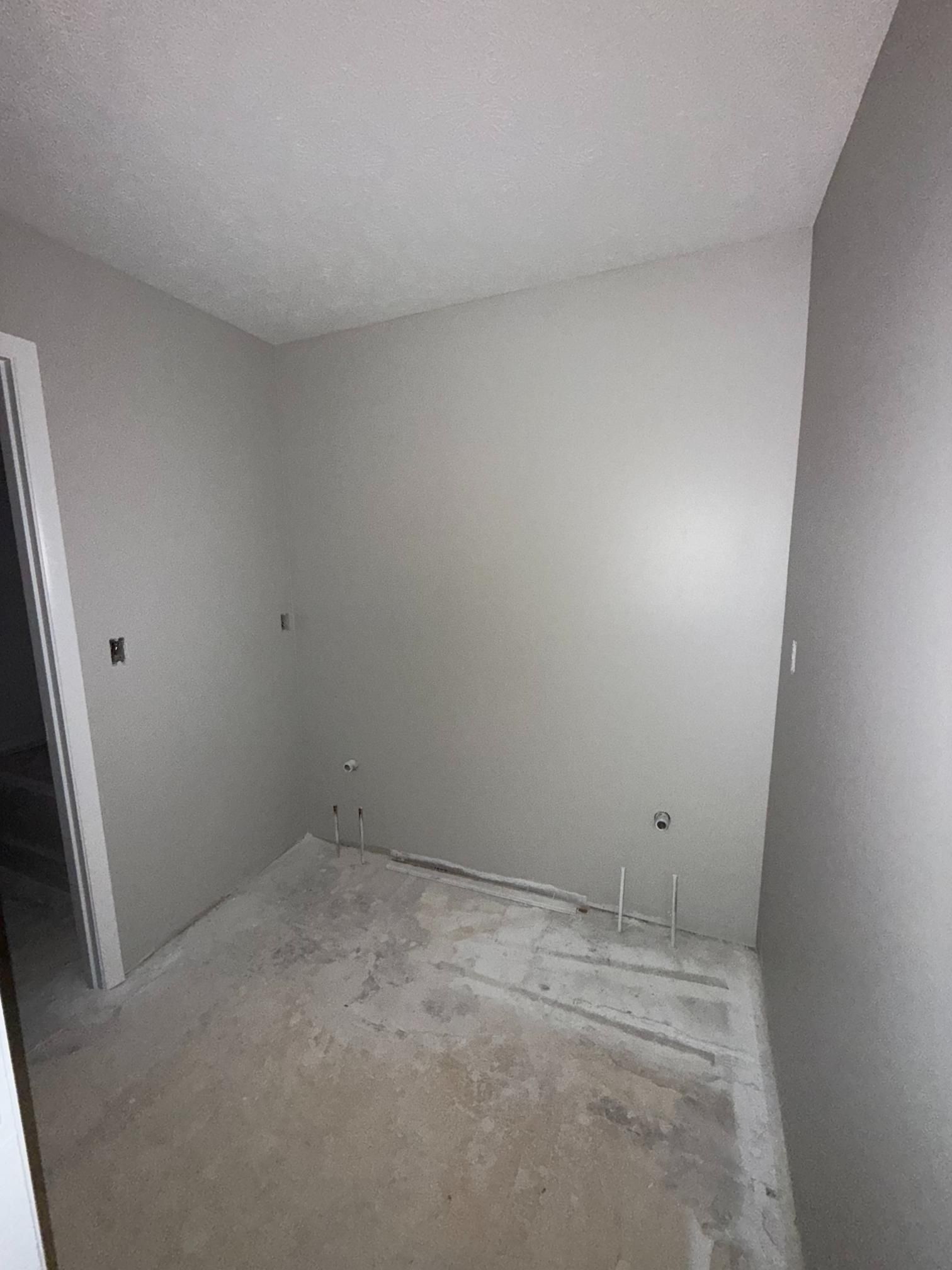 Empty room with gray walls and unfinished concrete floor; door and electrical outlets visible.