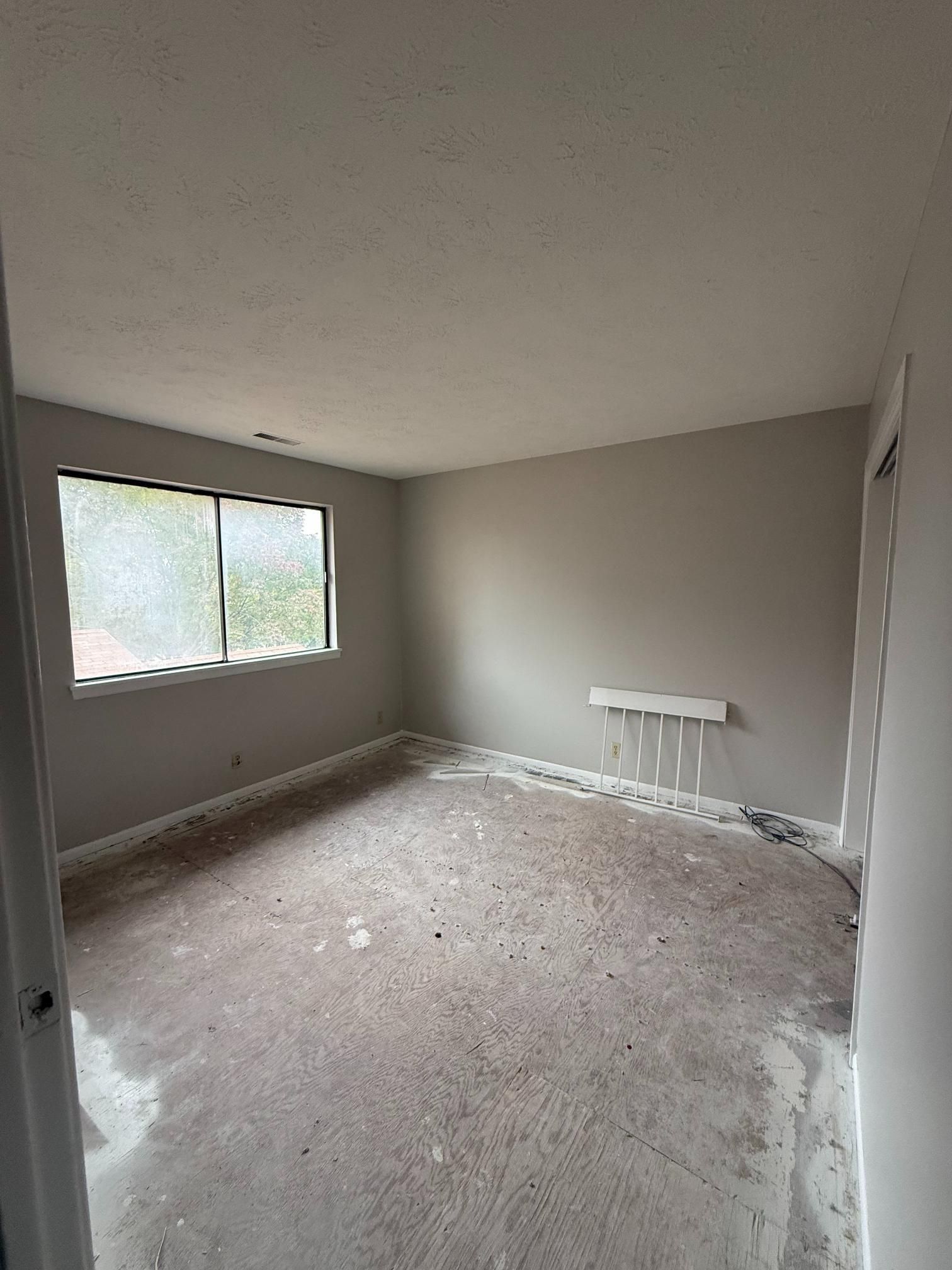 Empty room with gray walls and a window. Concrete floor is dirty.