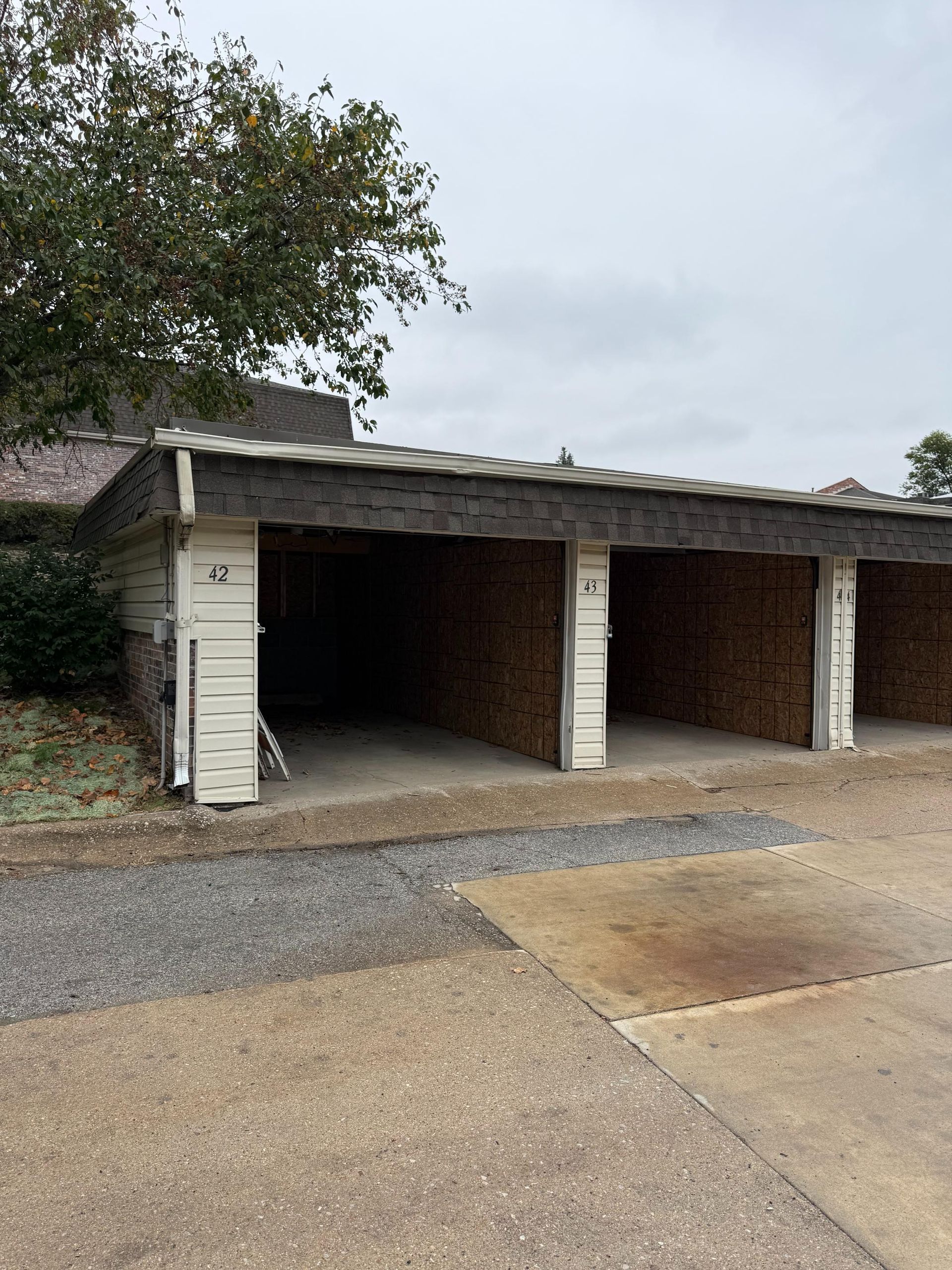 Three open-air parking stalls with brick walls, under a weathered roof, set on a concrete surface.