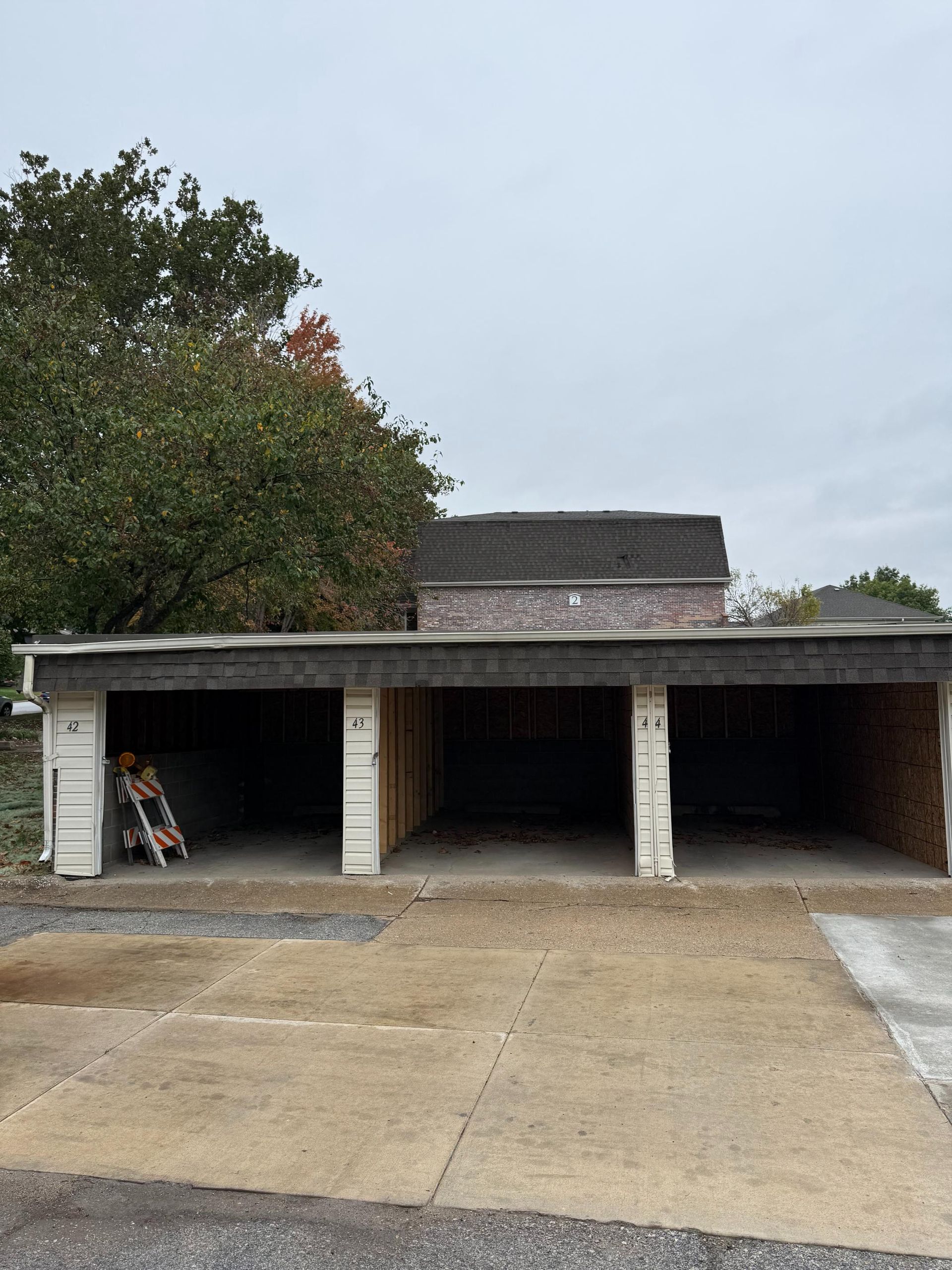 Three empty carport spaces with numbers, under a cloudy sky.