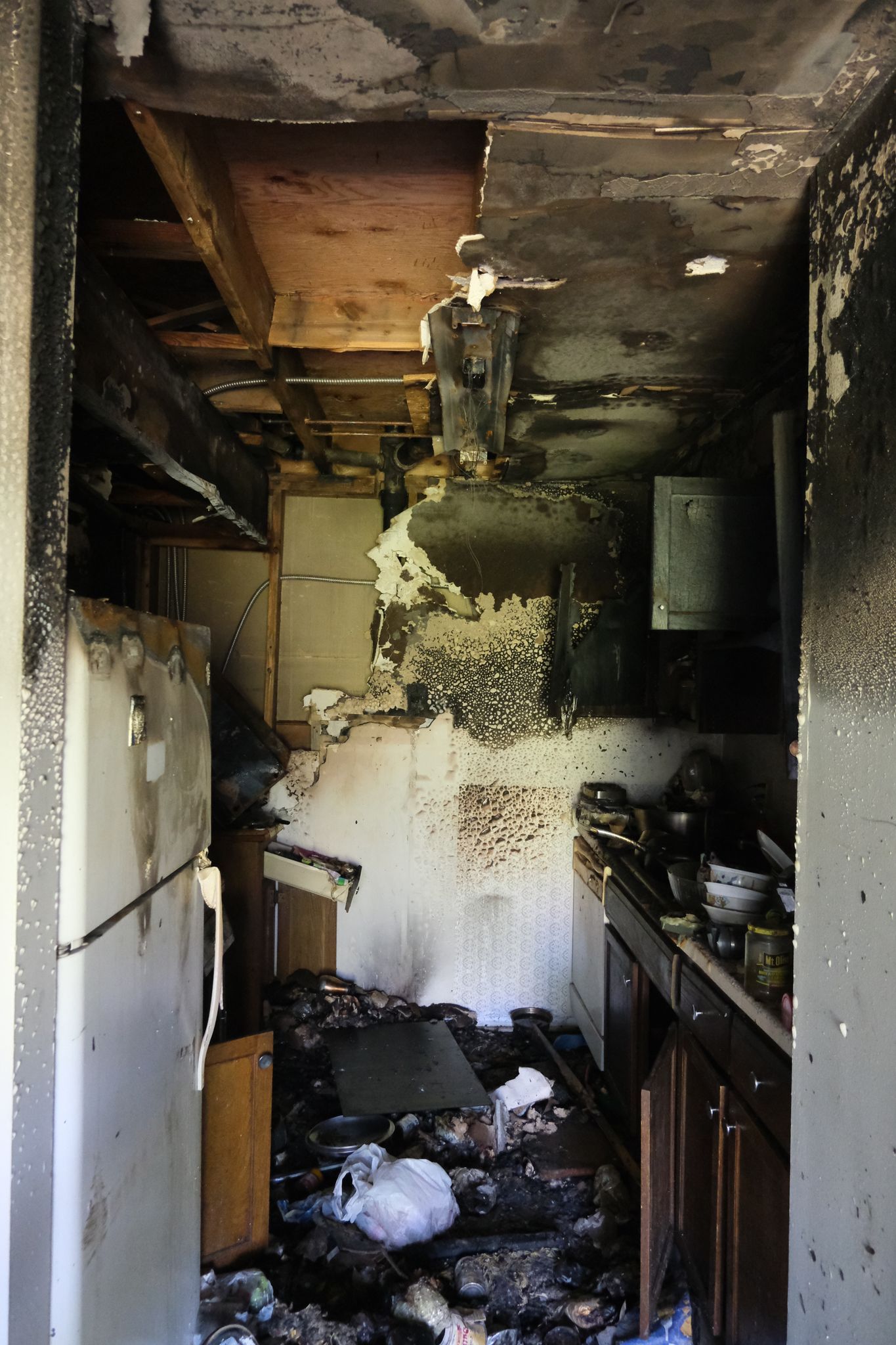 Charred interior of a kitchen after a fire. Burnt ceiling, appliances, and debris on the floor.