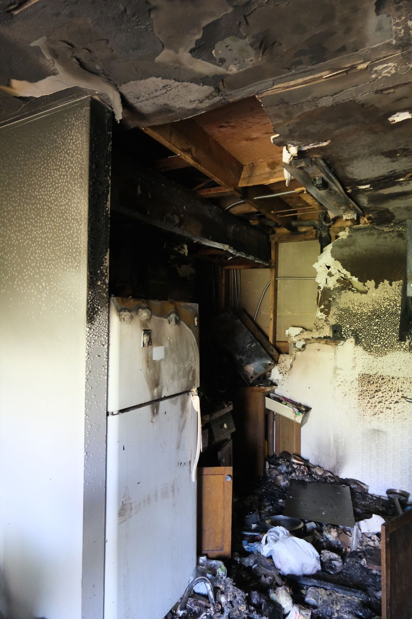 Interior of a kitchen severely damaged by fire; walls blackened, appliances charred, and debris strewn.