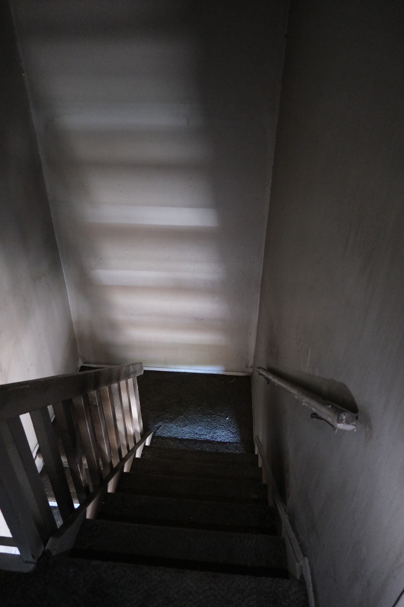 Staircase descending into shadow. Light from above casts stripes on the steps and wall.