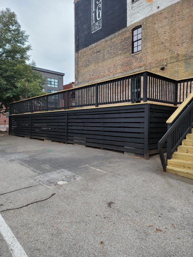 A black deck with stairs leading up to it is in front of a building.