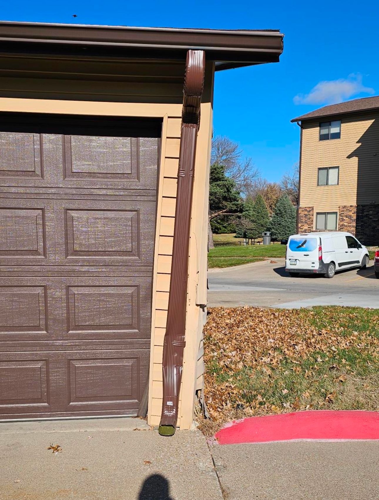 A brown garage door is next to a white van parked on the side of the road.