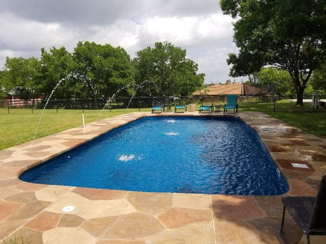 A large swimming pool is surrounded by chairs and trees.