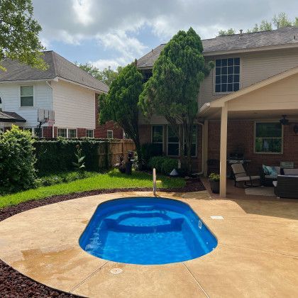 A small swimming pool is in the backyard of a house.