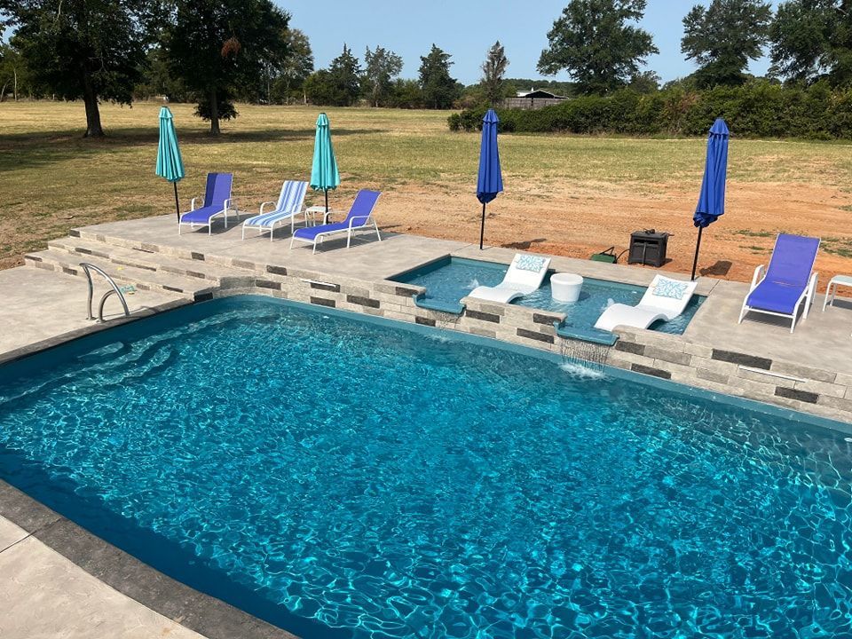 There is a large swimming pool in the backyard with chairs and umbrellas.