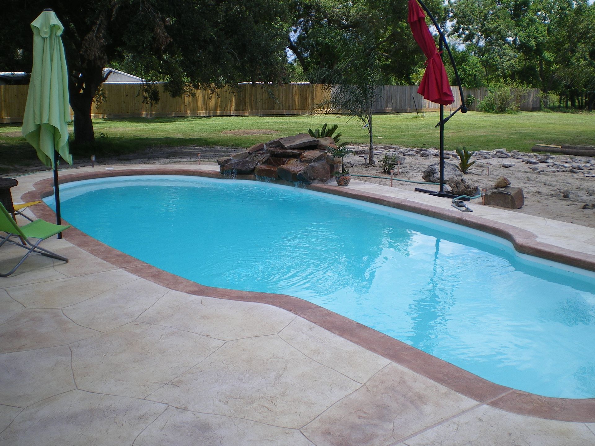 A swimming pool with a green umbrella and a red umbrella