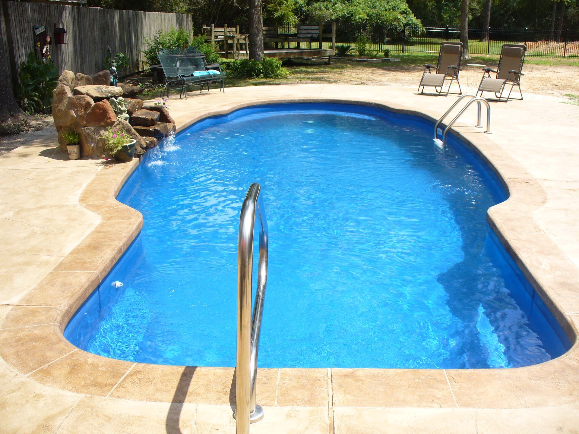 A large blue swimming pool with a waterfall in the backyard.