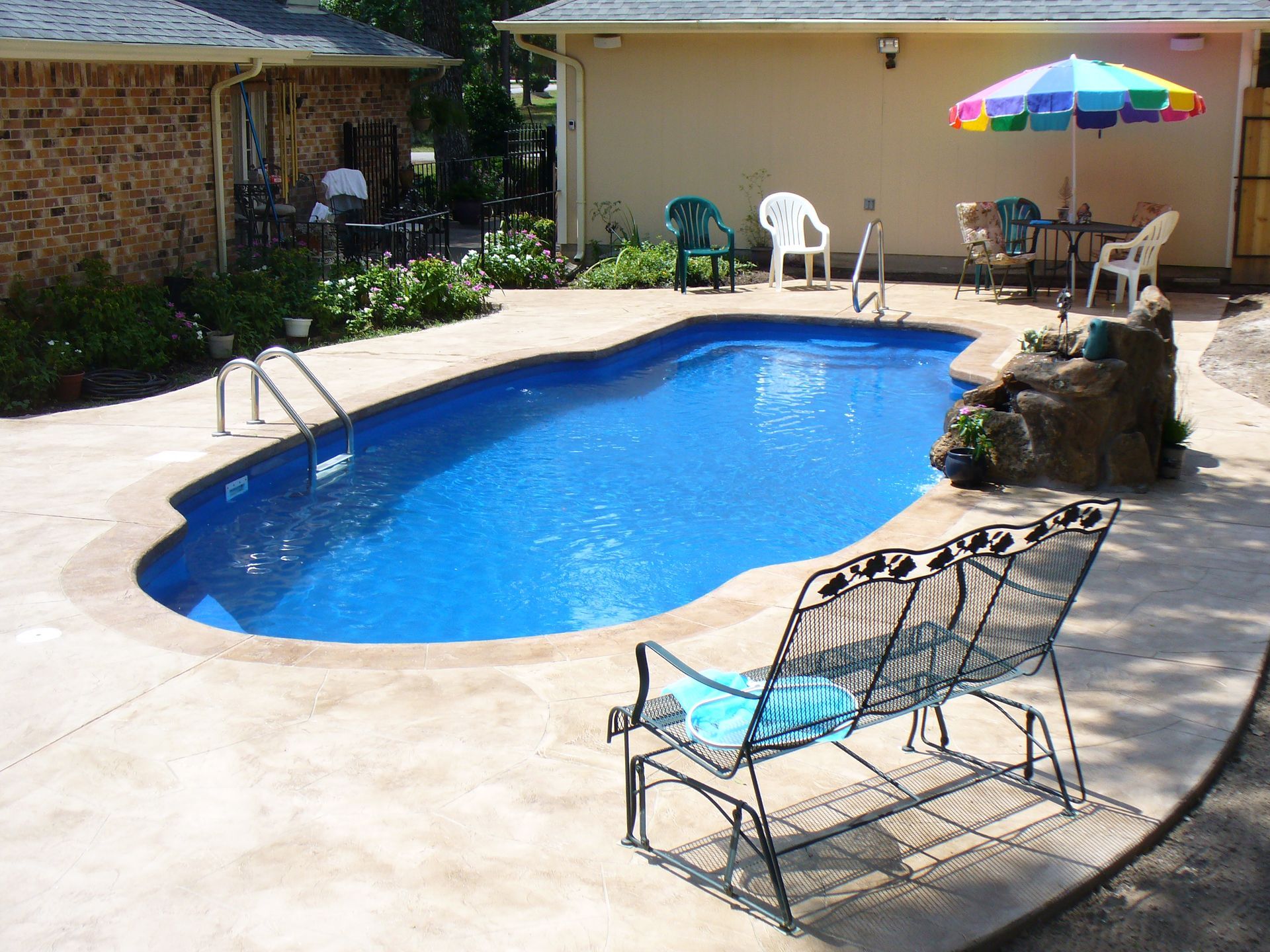 A swimming pool with a bench and umbrella in front of a house
