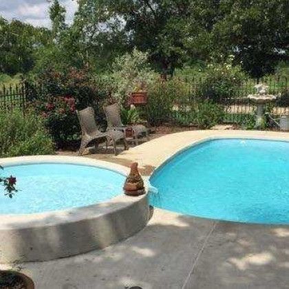 There are two swimming pools in the backyard with chairs and a fountain.