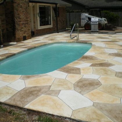 A swimming pool is surrounded by a patio with a bobcat in the background