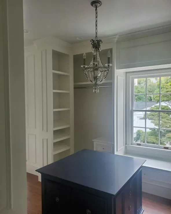 Walk-in closet with white shelves, window, dark blue island, and chandelier.