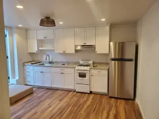 White kitchen with cabinets, stove, refrigerator, and wood-look flooring.