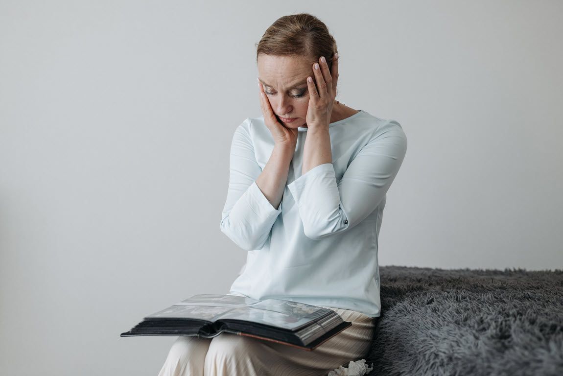 Woman sitting on a couch with hands on her face, looking distressed, with an open book on her lap