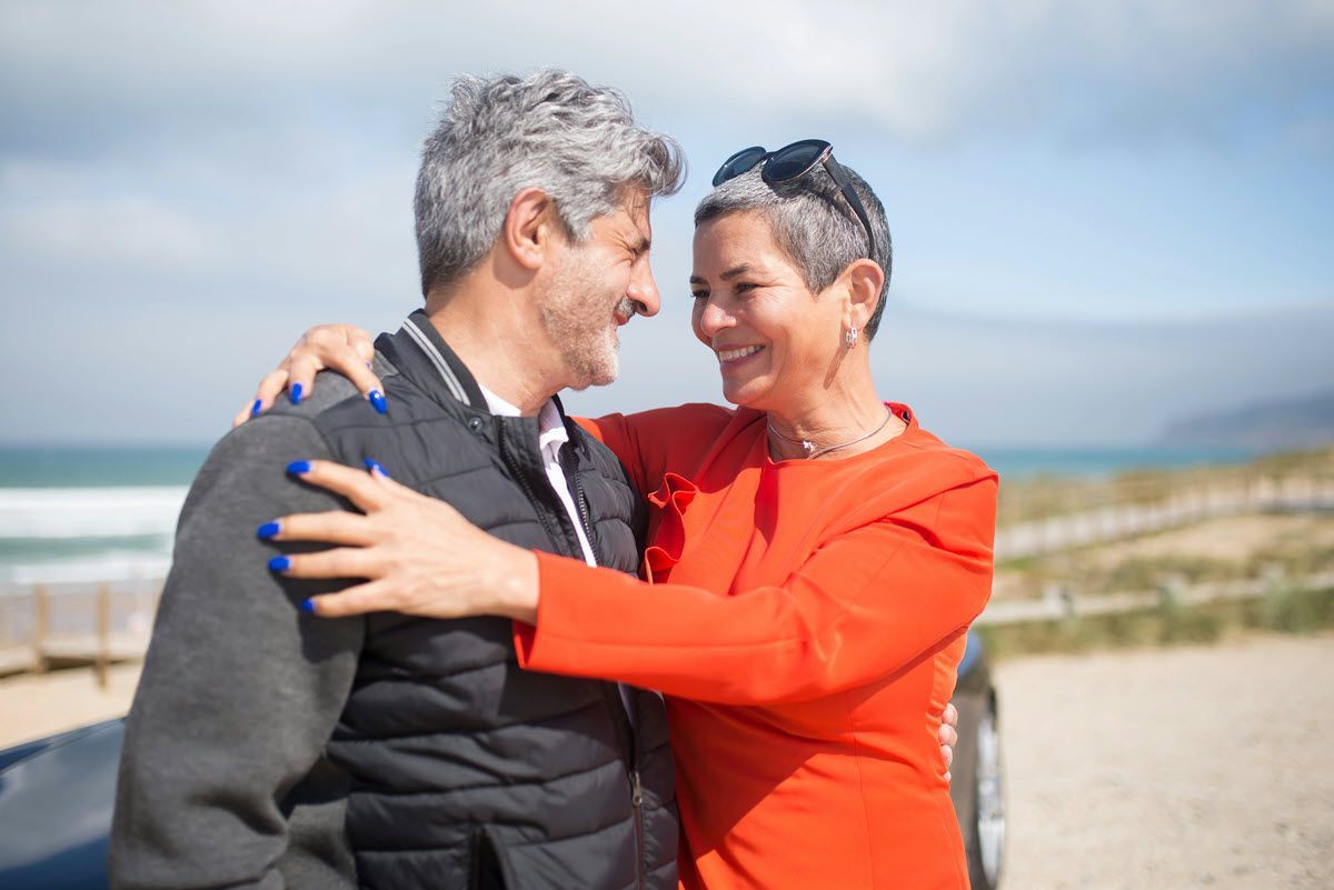 Two people smiling and embracing outdoors by the beach on a sunny day