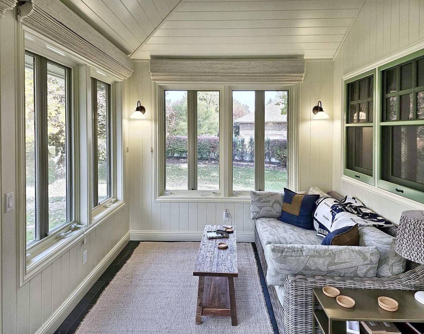 Four-season sun porch with painted tongue and groove walls, a vaulted paneled ceiling, windows on three sides, and green interior windows looking into the bedroom.