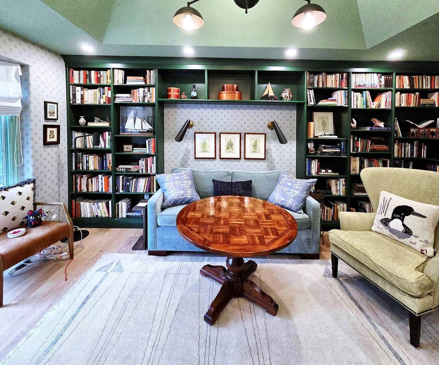 Library with built-in bookshelves painted deep green, wall sconces, patterned wallpaper, and white oak floors.