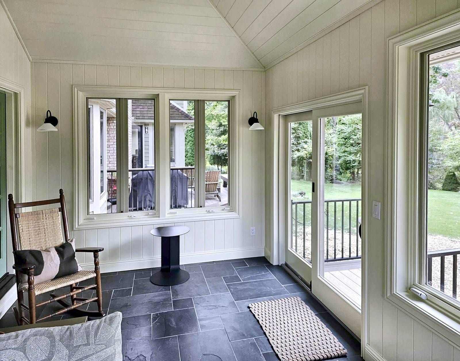 Sun porch with a rocking chair, slate tile floor, black wall sconces, and a glass door out to the deck.