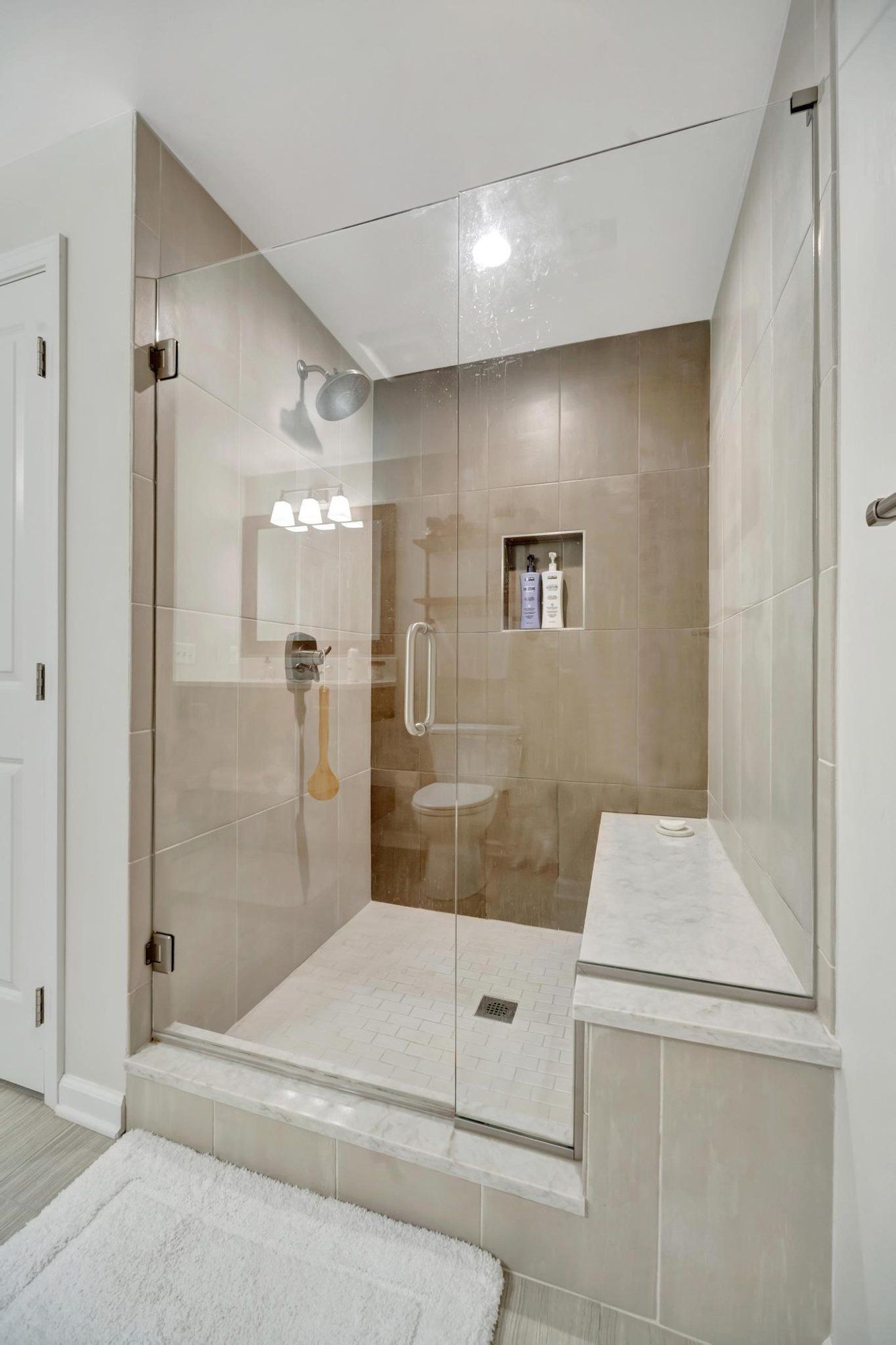 Basement bathroom walk-in shower with large format tile, a bench, and frameless glass.