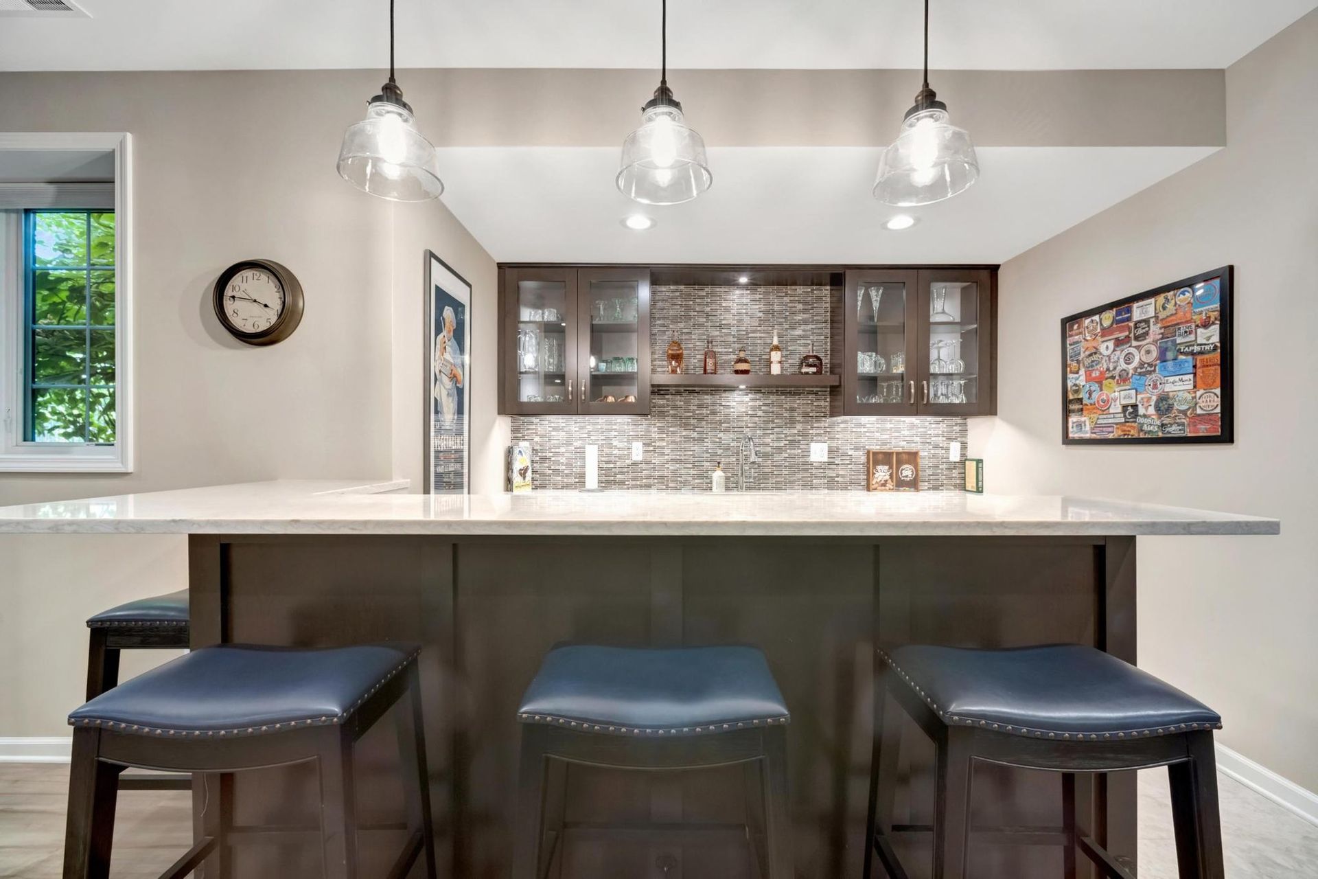 Basement wet bar with dark cherry cabinets, glass-front uppers, a mosaic backsplash, and a peninsula with stools.