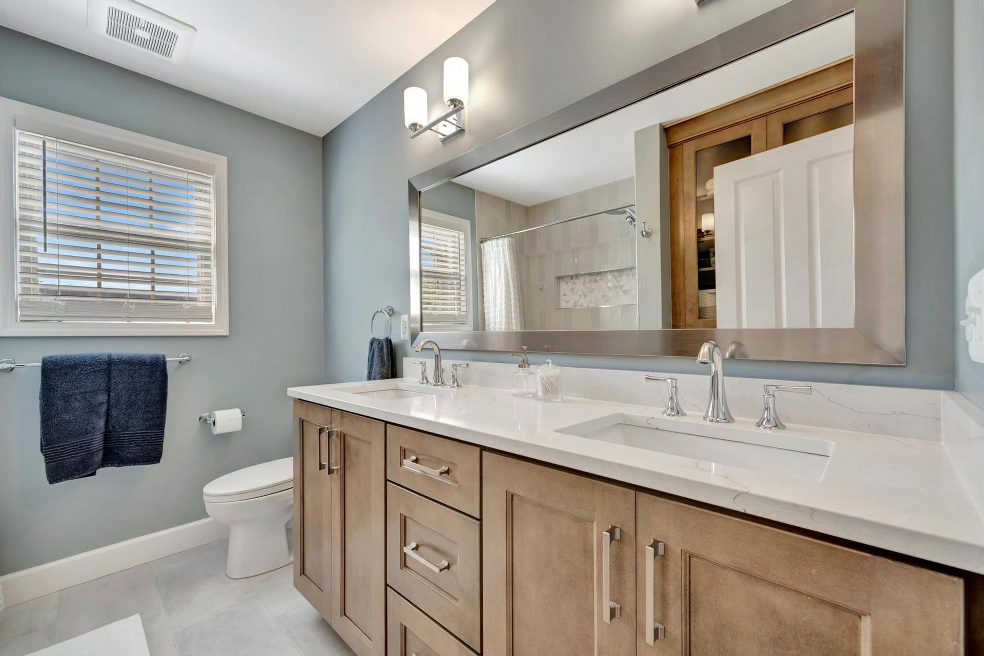 Family bathroom double vanity with stained shaker cabinets, a white quartz top, and chrome faucets.