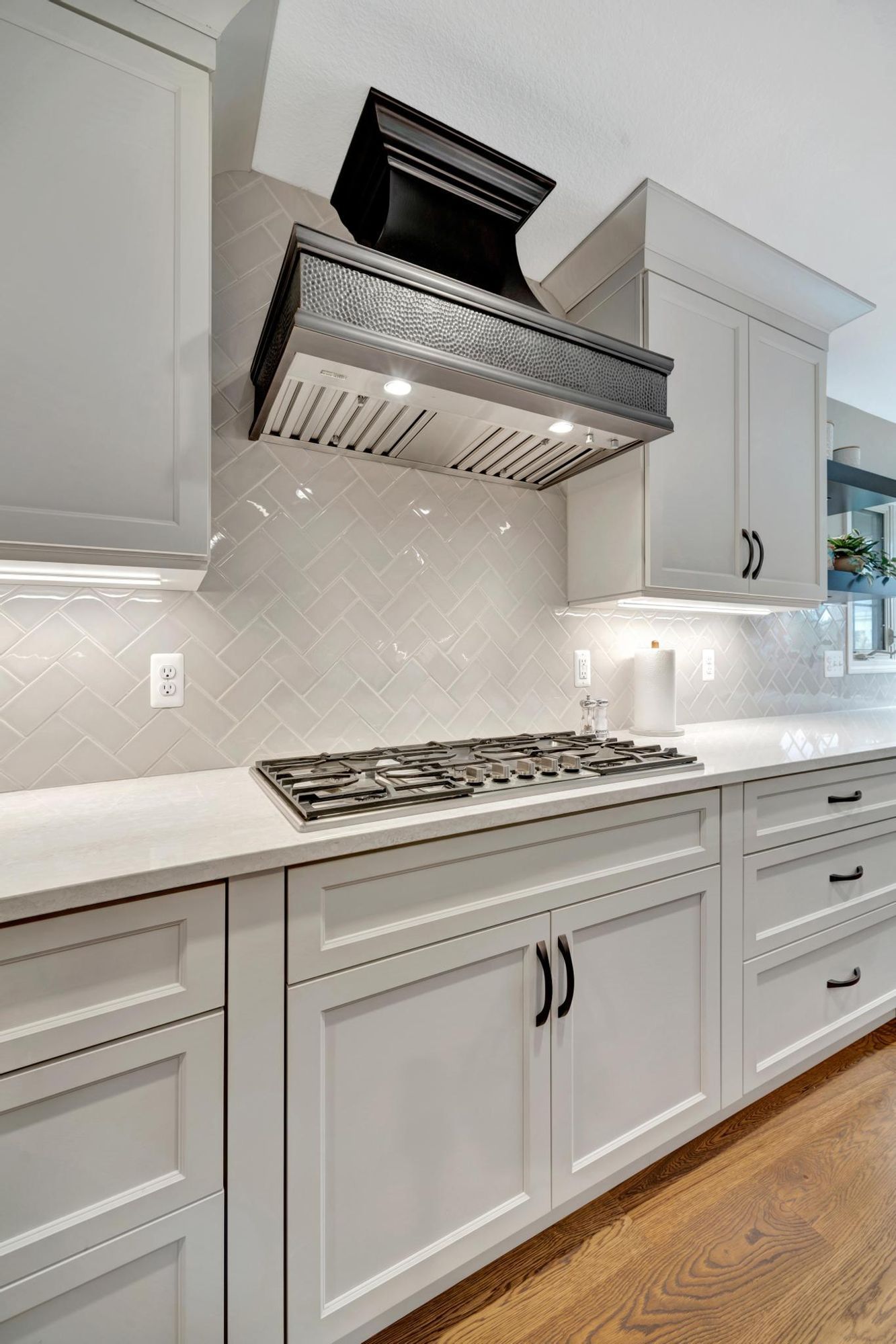 Hammered copper range hood over a gas cooktop with a glossy white herringbone tile backsplash.