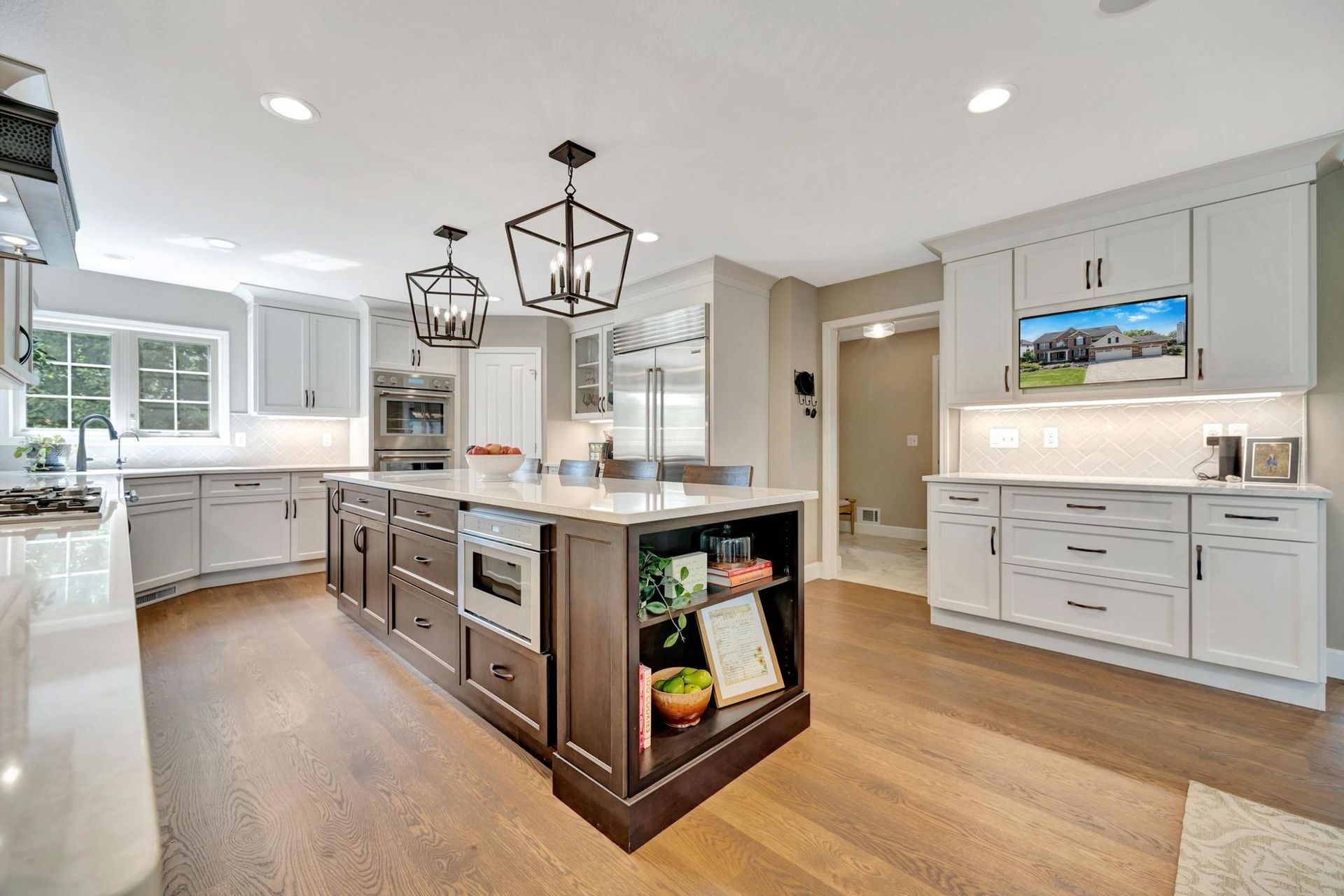 Remodeled kitchen with a stained island, white quartz countertops, black lantern pendants, a built-in refrigerator, and double wall ovens.