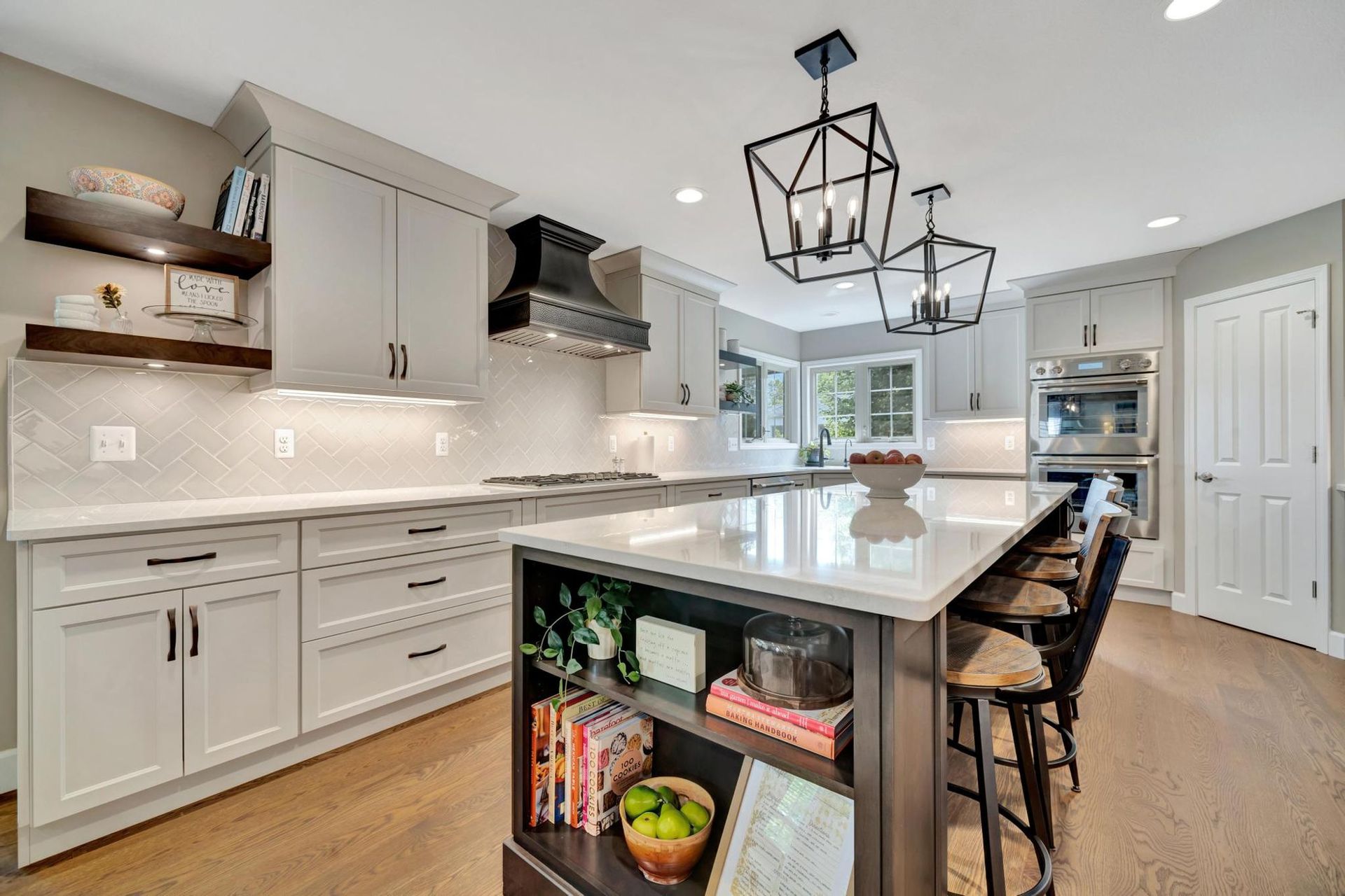 Kitchen range wall with light gray shaker cabinets, a hammered copper range hood, white herringbone tile, and walnut floating shelves.