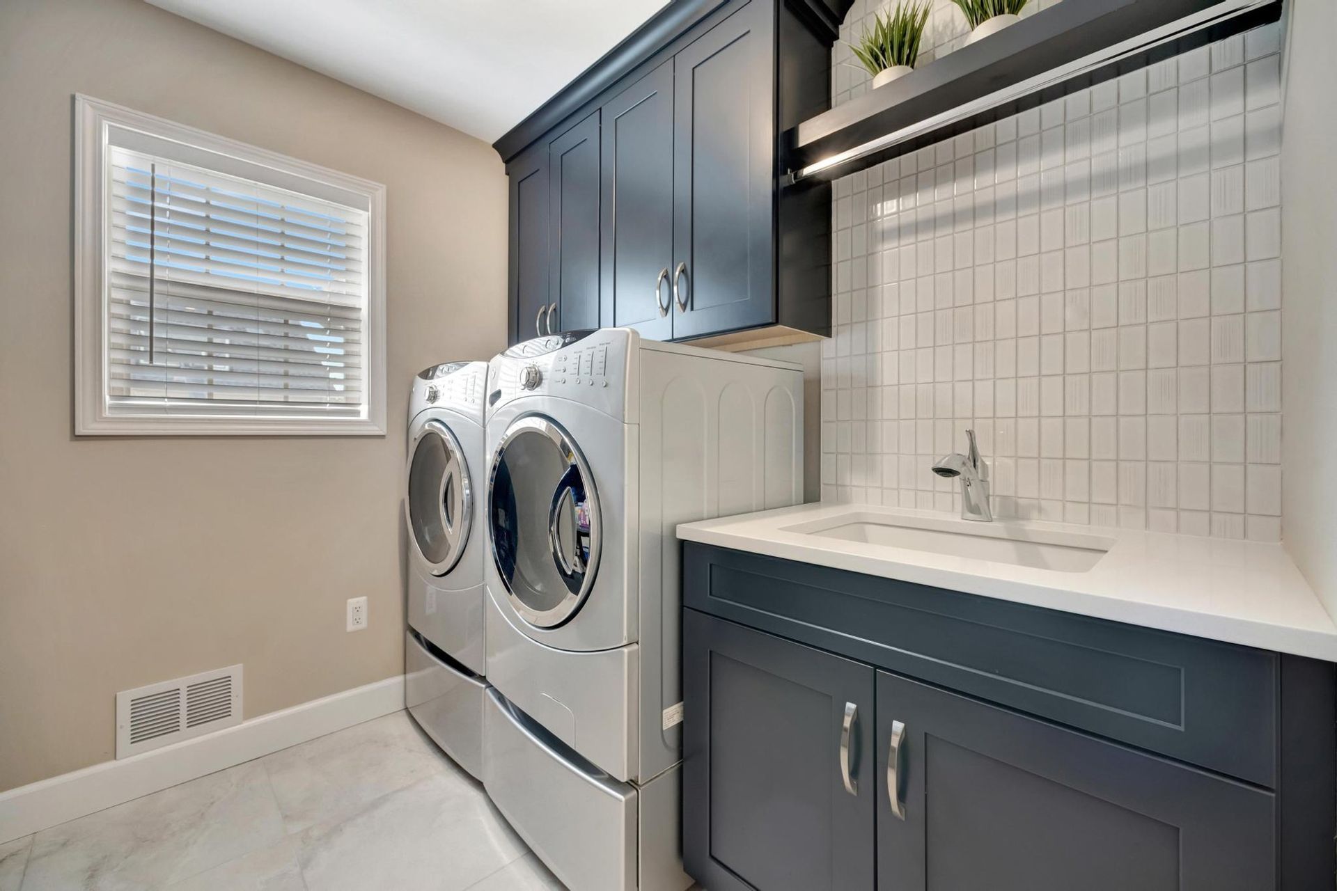 Laundry room with navy shaker cabinets, a white quartz counter with a laundry sink, and a white tile backsplash.
