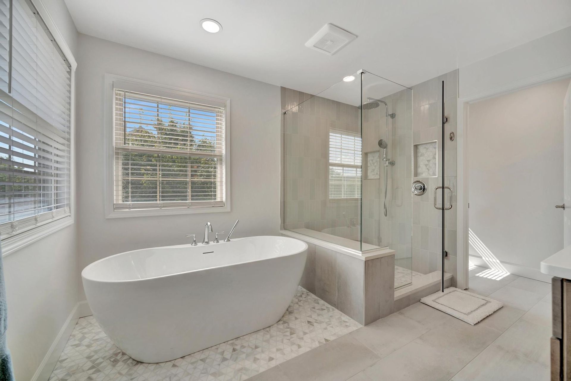 Primary bathroom with a freestanding soaking tub on marble mosaic tile and a frameless glass walk-in shower.