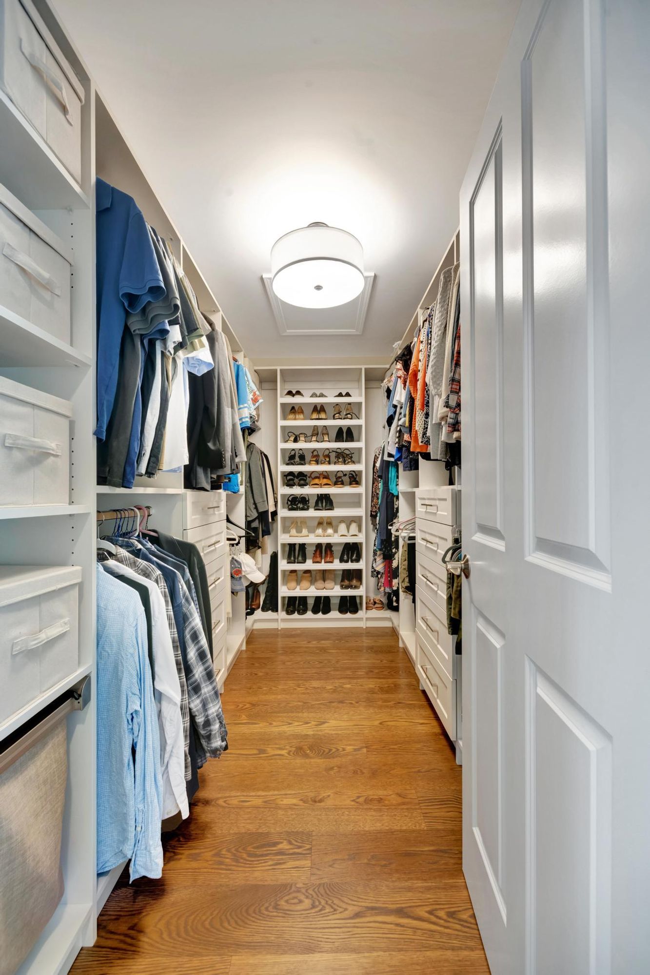 Primary walk-in closet with a white built-in closet system, drawers, and shoe shelves.