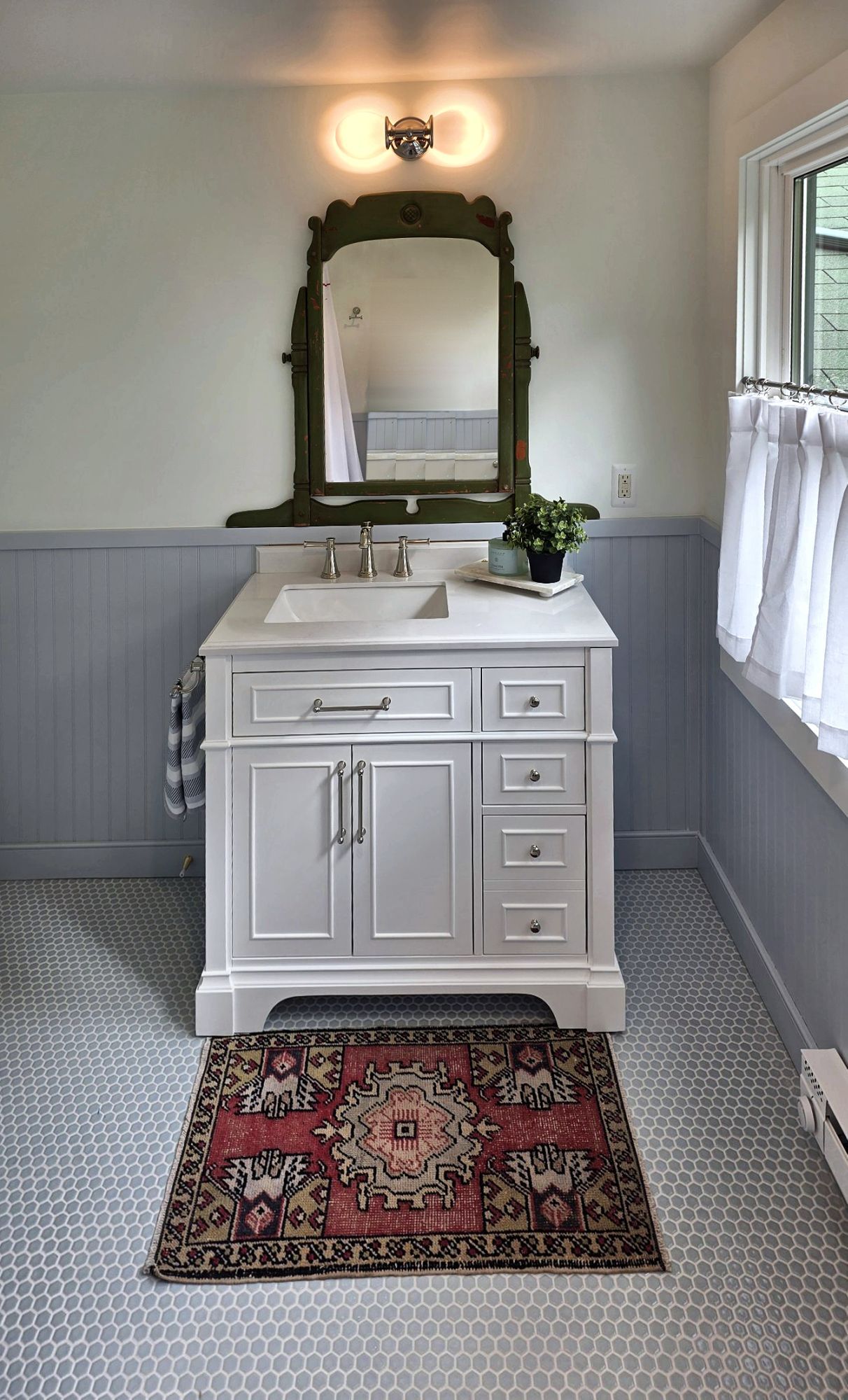 Bathroom with a white single vanity, blue-gray beadboard wainscot, and a penny tile floor.