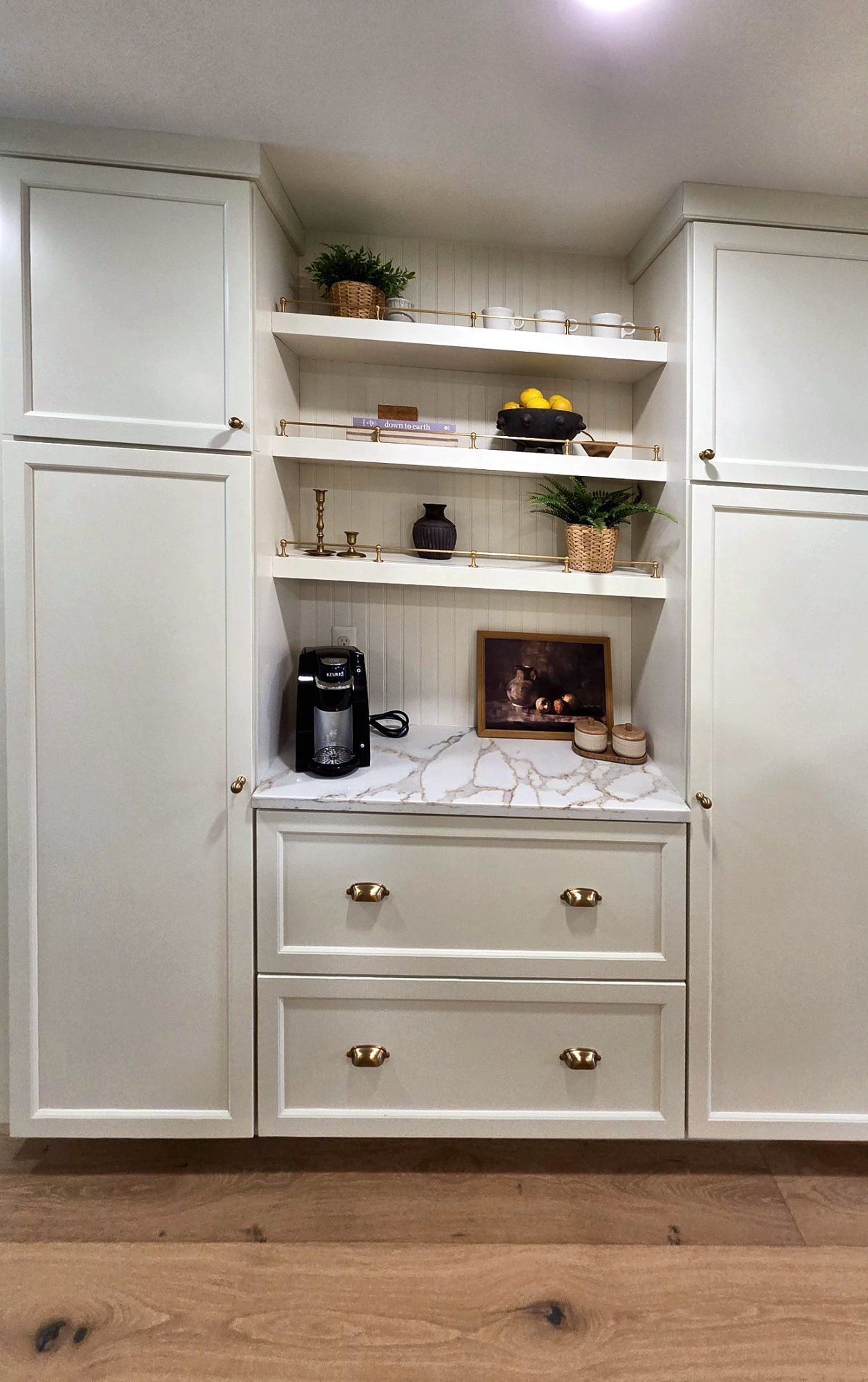 Built-in coffee station between tall white pantry cabinets, with open shelves on a beadboard back and brass gallery rails.