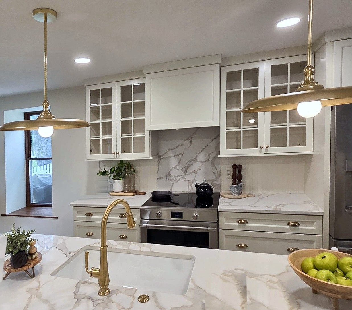 Remodeled kitchen with a white island sink, brass pendant lights, white quartz countertops with gold veining, and glass-front upper cabinets.
