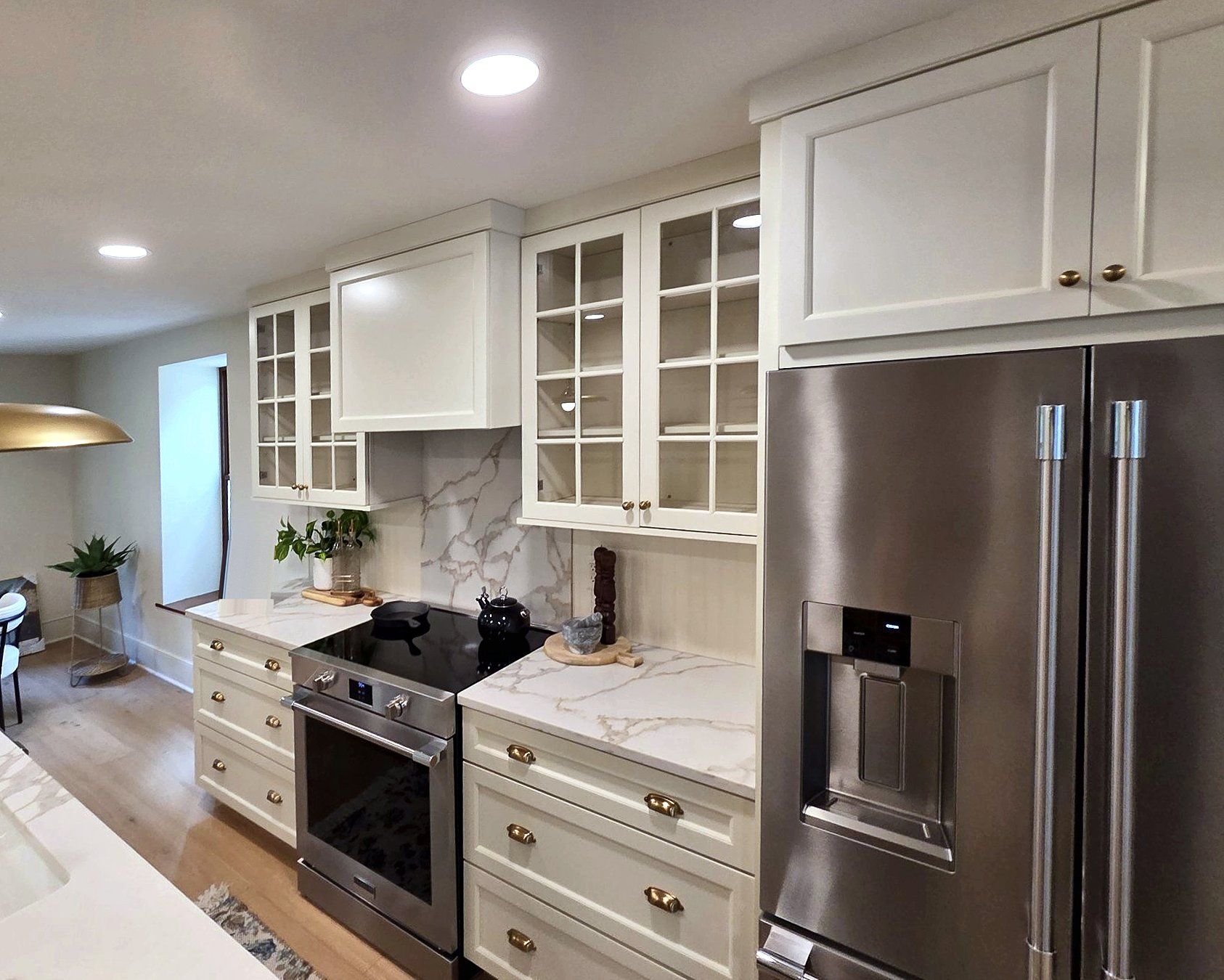 Kitchen range wall with white shaker cabinets, glass-front uppers, a quartz slab backsplash, and a stainless French door refrigerator.
