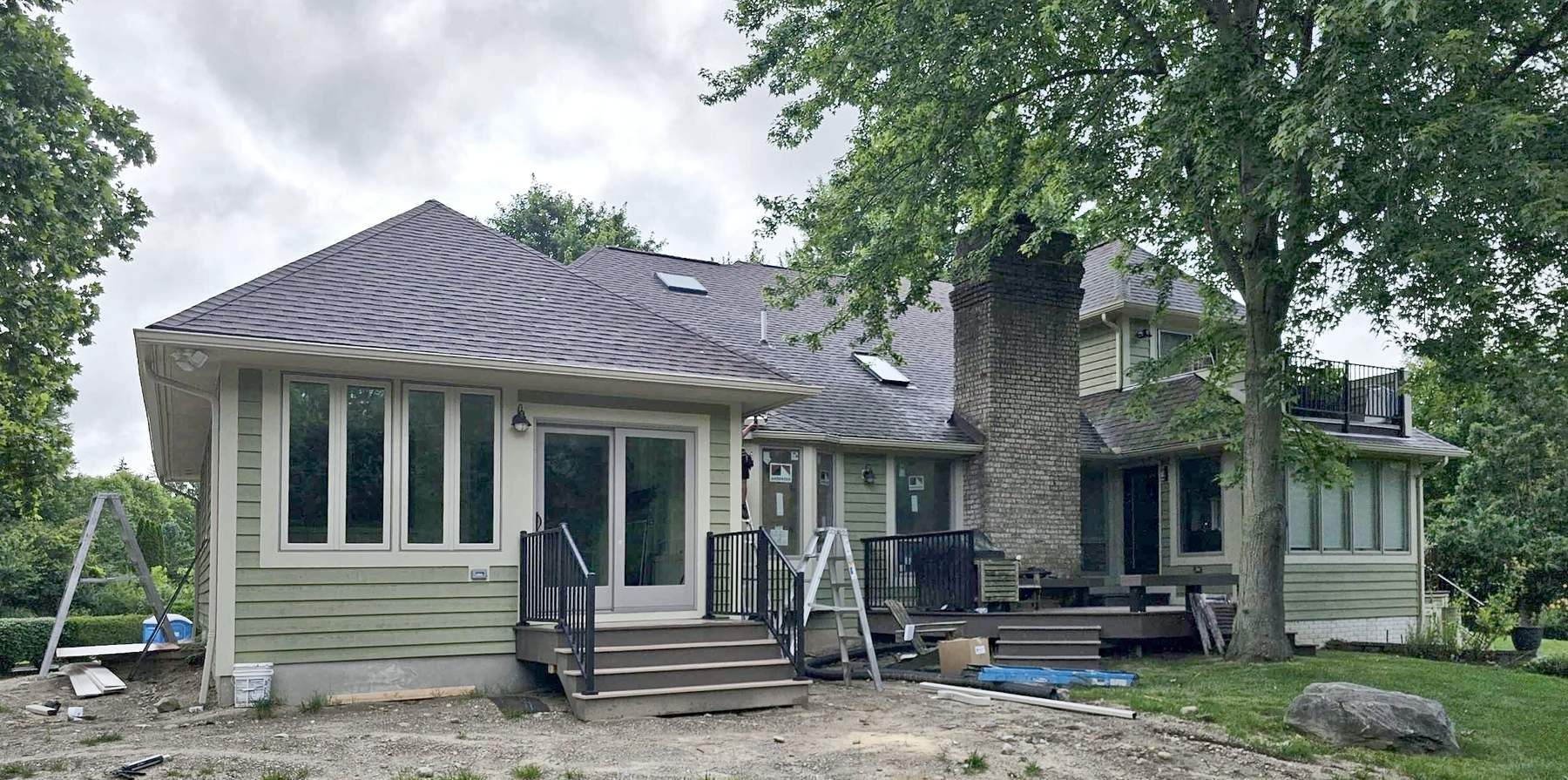Back of the finished addition with green lap siding, sun porch windows, a glass patio door, and new deck stairs.