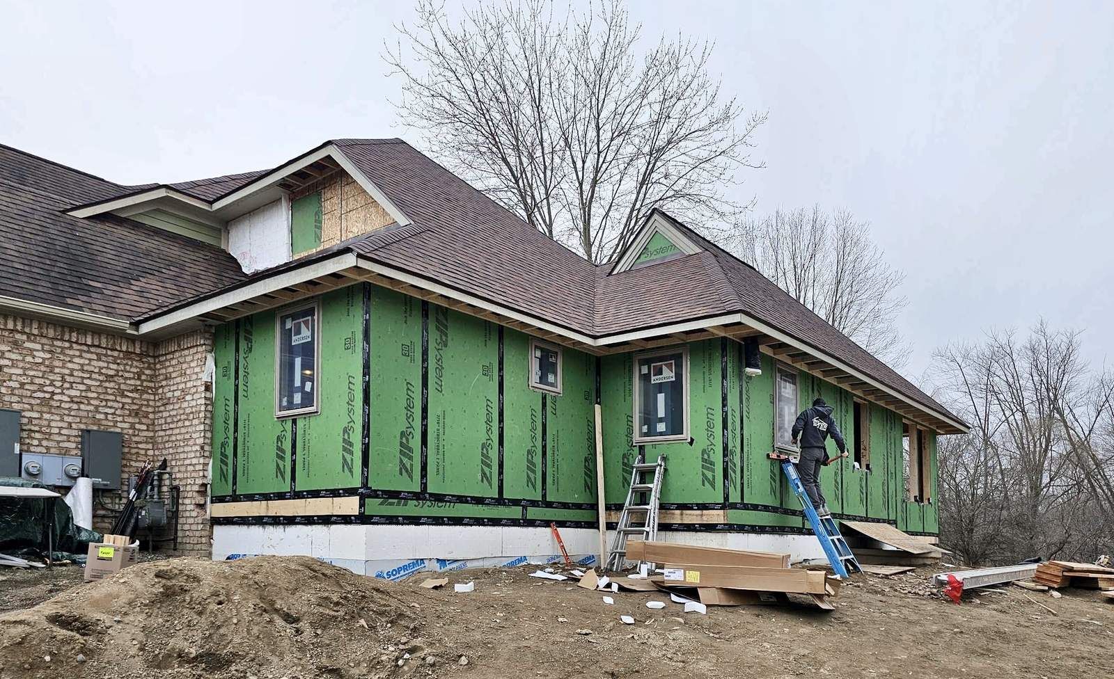 Home addition framed and sheathed in green Zip System panels, with a carpenter working from a ladder.