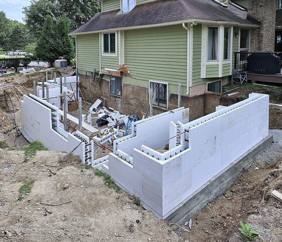 Insulated concrete form (ICF) basement walls going up for a home addition, set on poured footings next to the existing house.