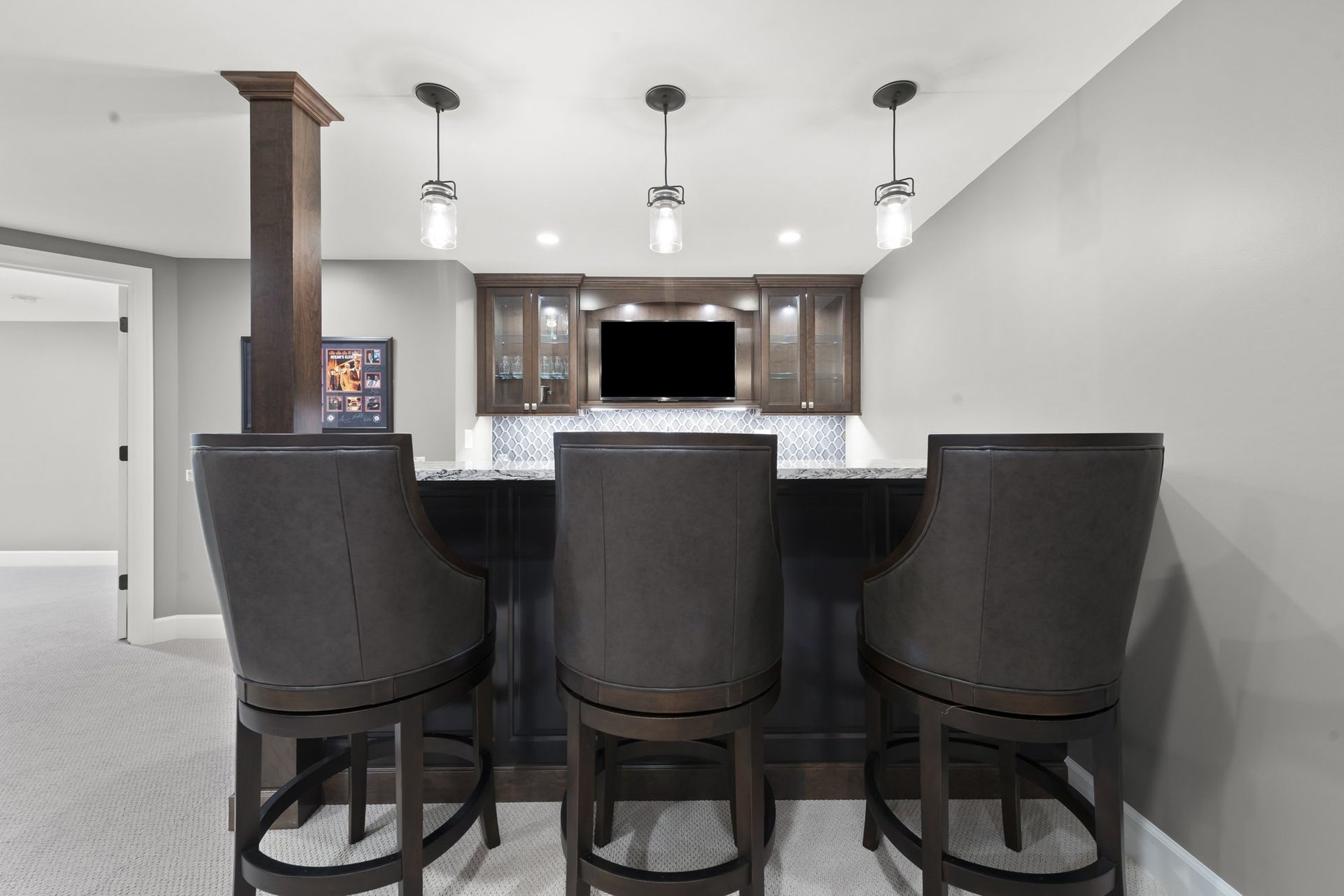 Basement wet bar with a wood-wrapped support column, glass-front cabinets, and a gray tile backsplash.