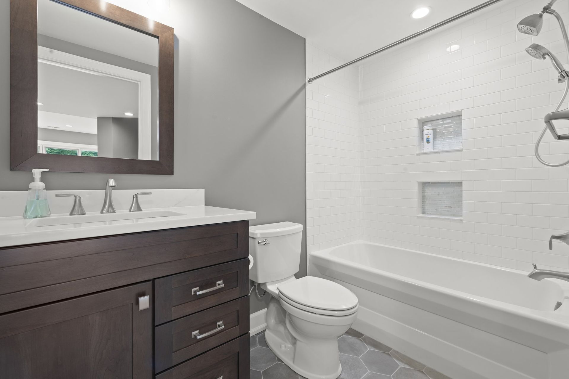 Basement full bathroom with an espresso vanity, white subway tile tub surround, and gray hexagon floor tile.