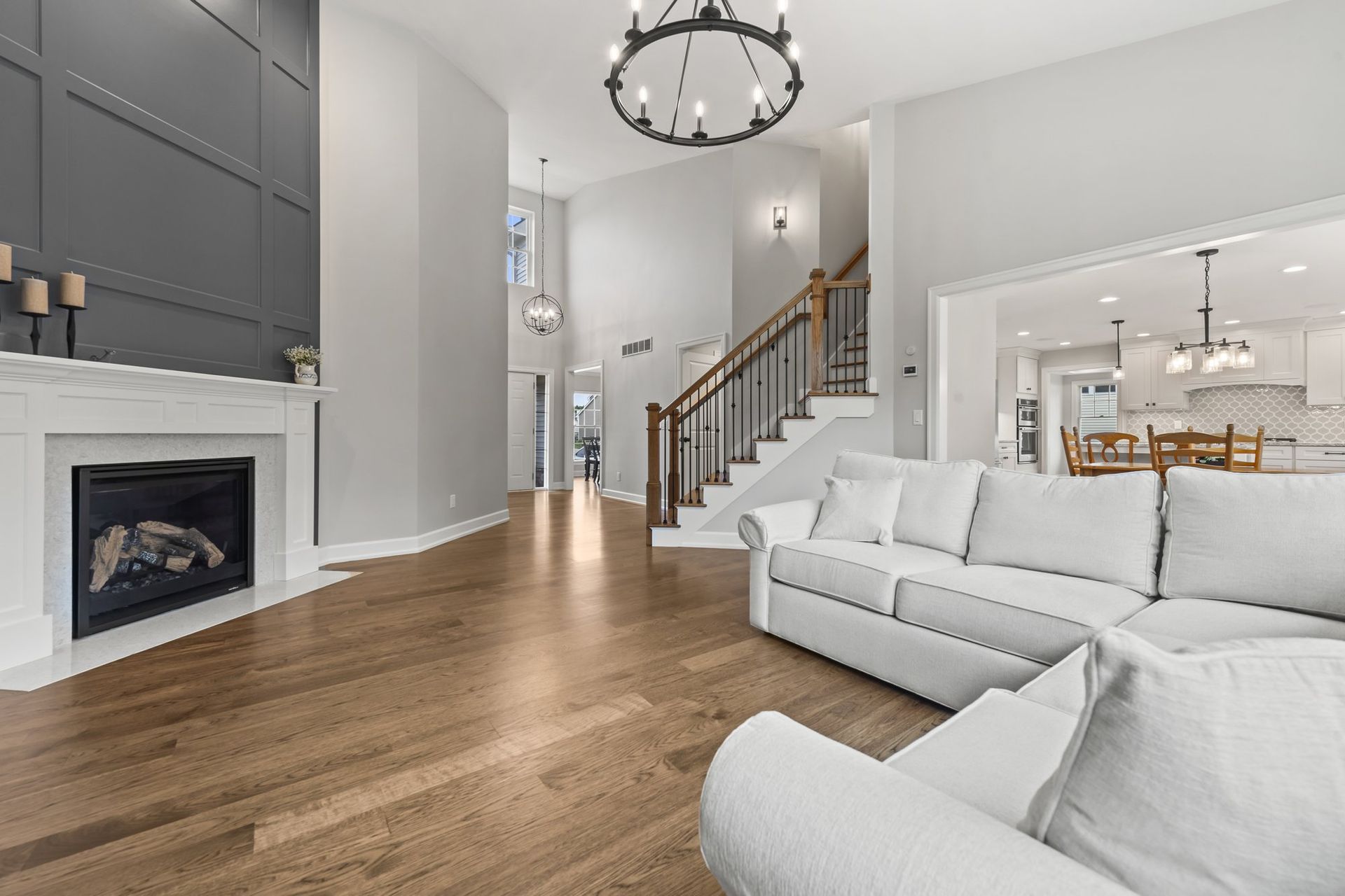 Family room with a gas fireplace, white mantel, and full-height gray paneled wall, looking toward the staircase and kitchen.