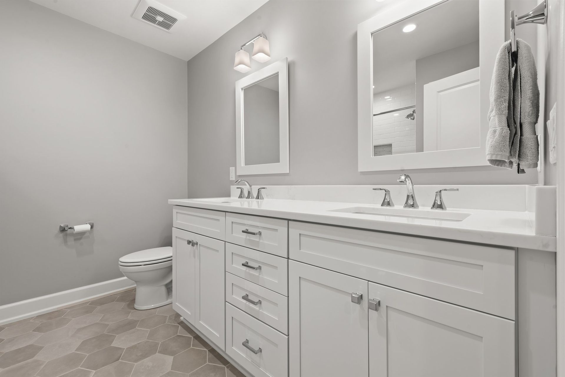 Hall bathroom with a white double vanity, framed mirrors, and large hexagon floor tile.