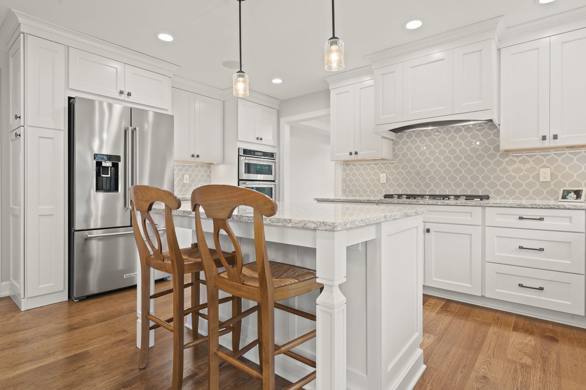 Kitchen island with rush seat stools in front of a refrigerator and double wall oven set into white cabinetry.