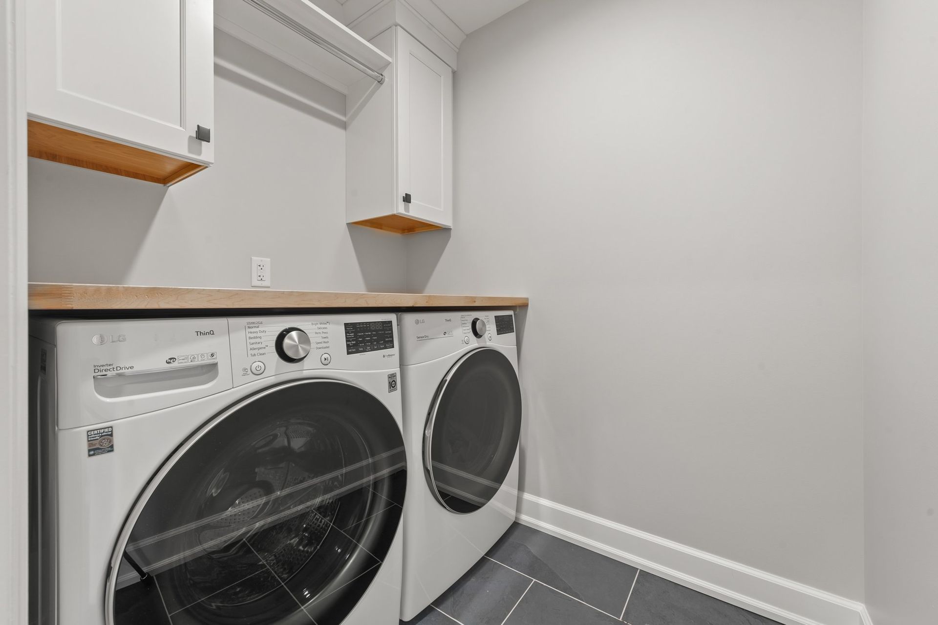 Second floor laundry room with a front-load washer and dryer under a wood counter and white upper cabinets.